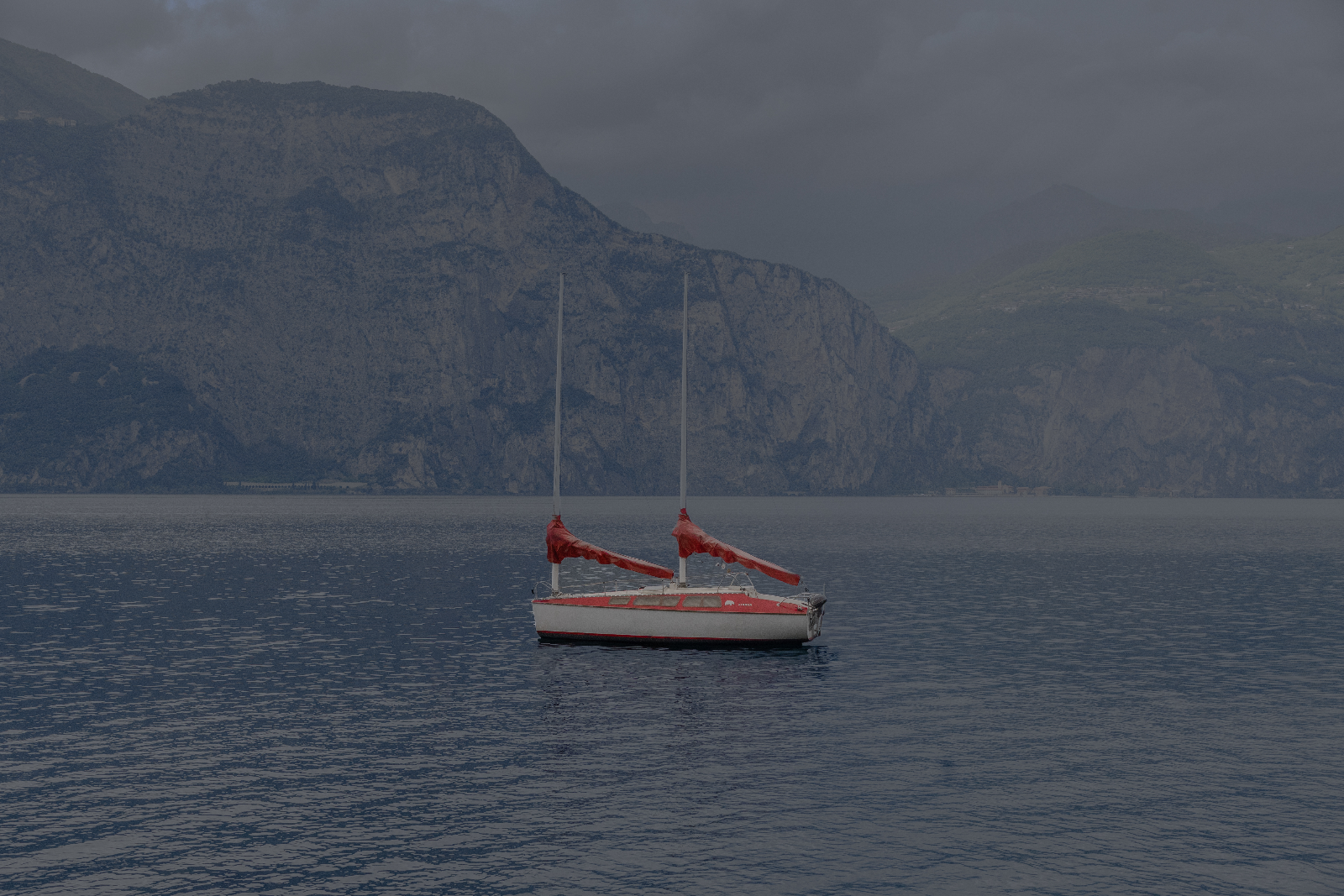 Voilier aux voiles rouges sur un lac gris