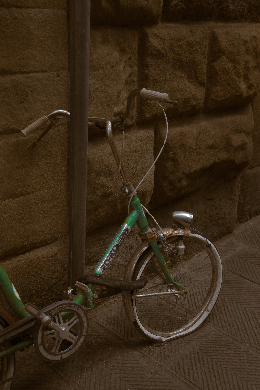 Vélo vert à la roue voilée contre un mur de pierre