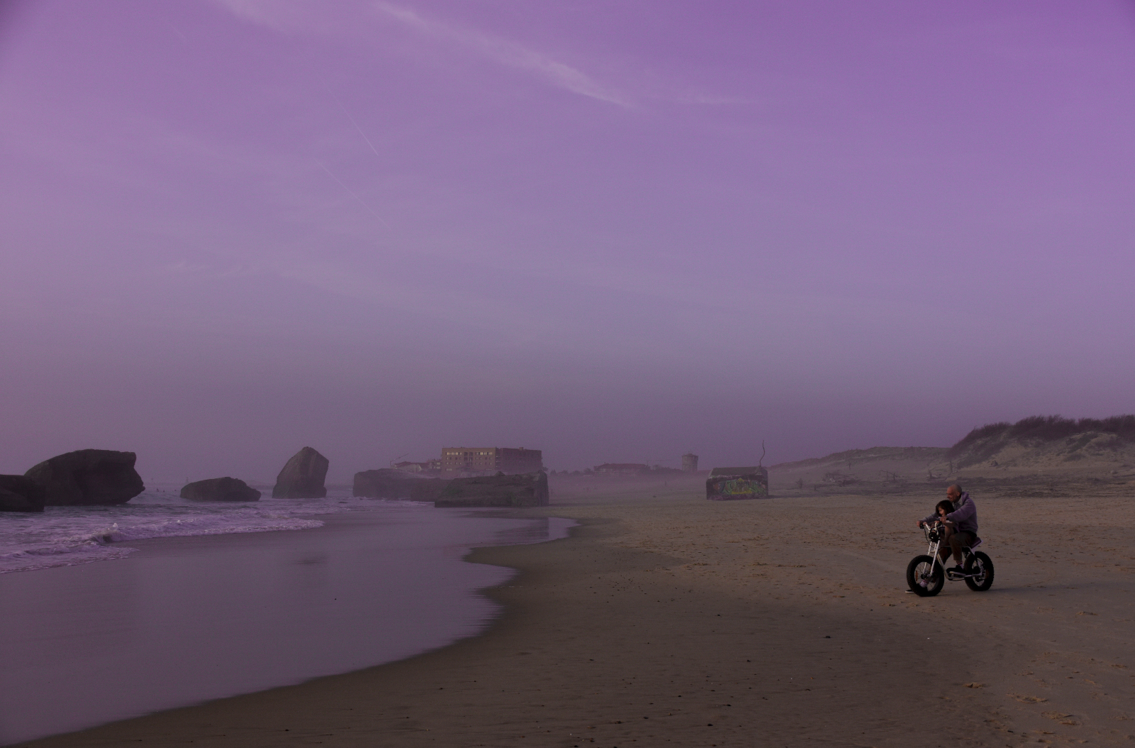 Plage brumeuse violette, homme et enfant à vélo
